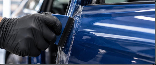 Clear paint protection film being applied to a blue car door edge with a squeegee